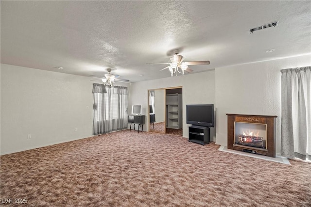 unfurnished living room featuring carpet floors, a ceiling fan, a fireplace with flush hearth, a textured ceiling, and visible vents