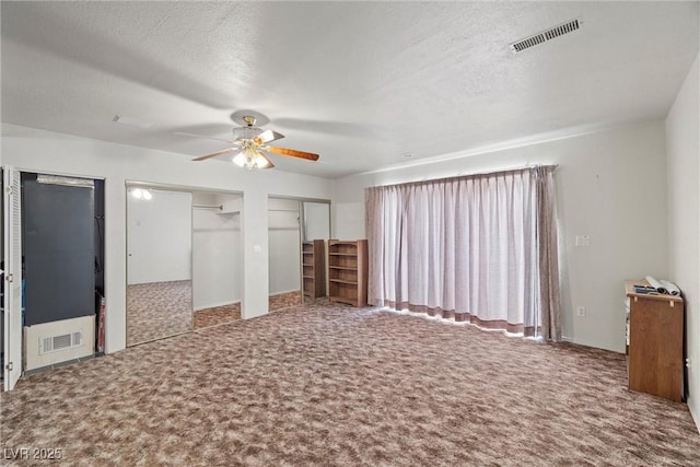 unfurnished bedroom featuring carpet floors, a textured ceiling, visible vents, and two closets
