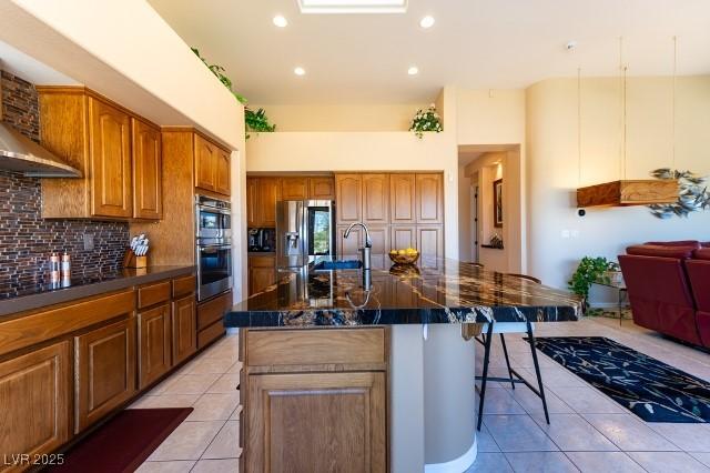 10524 Longwood Dr, Las Vegas, NV 89134 - kitchen featuring decorative backsplash, a breakfast bar, appliances with stainless steel finishes, brown cabinetry, and light tile patterned floors