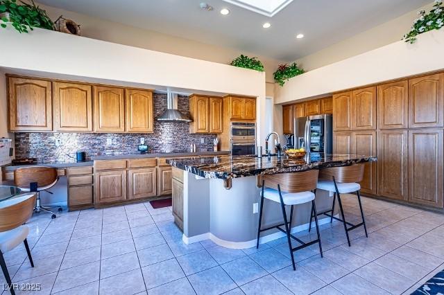 10524 Longwood Dr, Las Vegas, NV 89134 - kitchen with a breakfast bar area, stainless steel appliances, backsplash, wall chimney range hood, and brown cabinets