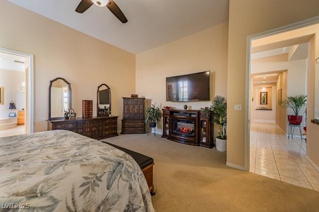 10524 Longwood Dr, Las Vegas, NV 89134 - bedroom with light tile patterned floors, connected bathroom, ceiling fan, light carpet, and a glass covered fireplace
