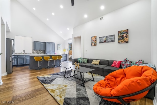 living room with light wood finished floors, visible vents, high vaulted ceiling, and recessed lighting