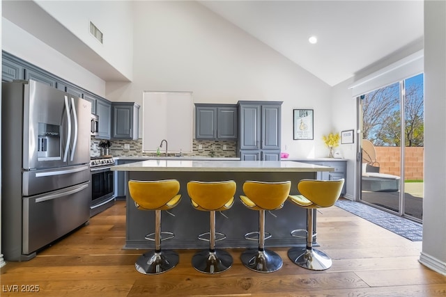 kitchen featuring light countertops, stainless steel appliances, visible vents, decorative backsplash, and dark wood-style flooring