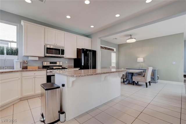 kitchen featuring light tile patterned floors, a center island, light stone counters, white cabinets, and appliances with stainless steel finishes