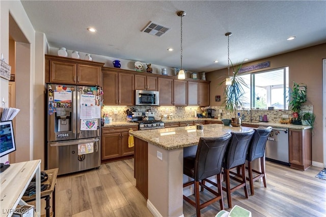 9511 Star Vista Ct, Las Vegas, NV 89149 - kitchen featuring stainless steel appliances, light wood-type flooring, tasteful backsplash, a kitchen island, and light stone countertops