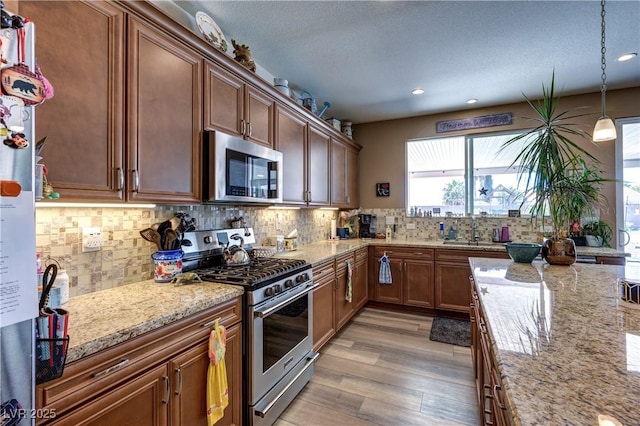 9511 Star Vista Ct, Las Vegas, NV 89149 - kitchen with appliances with stainless steel finishes, light wood-style floors, decorative backsplash, light stone counters, and pendant lighting