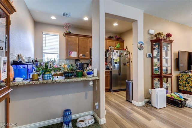 9511 Star Vista Ct, Las Vegas, NV 89149 - kitchen with stainless steel fridge with ice dispenser, light wood-type flooring, brown cabinetry, light stone counters, and tasteful backsplash