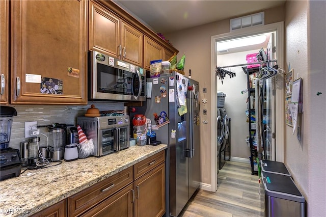9511 Star Vista Ct, Las Vegas, NV 89149 - kitchen with stainless steel appliances, washer and clothes dryer, backsplash, light wood-type flooring, and brown cabinets