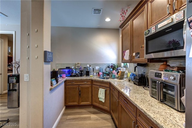 9511 Star Vista Ct, Las Vegas, NV 89149 - kitchen with a sink, stainless steel microwave, light wood-style floors, light stone counters, and brown cabinetry