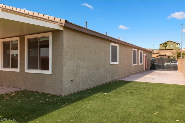 exterior space with a gate, a patio, stucco siding, and a yard