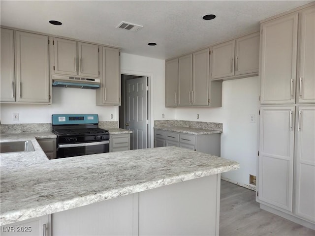 kitchen featuring stainless steel range with gas stovetop, a peninsula, visible vents, under cabinet range hood, and light countertops