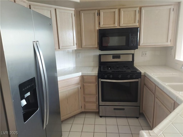kitchen with light brown cabinetry, tile countertops, a sink, backsplash, and stainless steel appliances