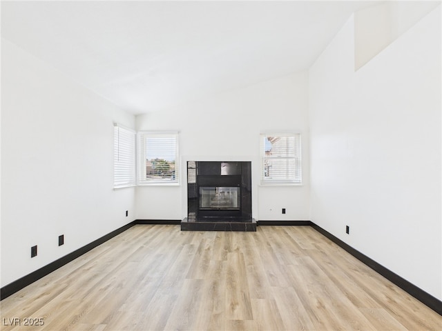 unfurnished living room with baseboards, a tile fireplace, a healthy amount of sunlight, and wood finished floors