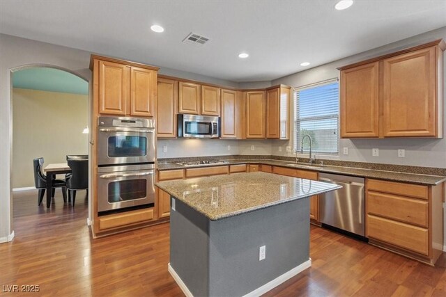 640 Finch Island Ave, Henderson, NV 89015 - kitchen with dark wood-style flooring, appliances with stainless steel finishes, a sink, arched walkways, and dark stone countertops
