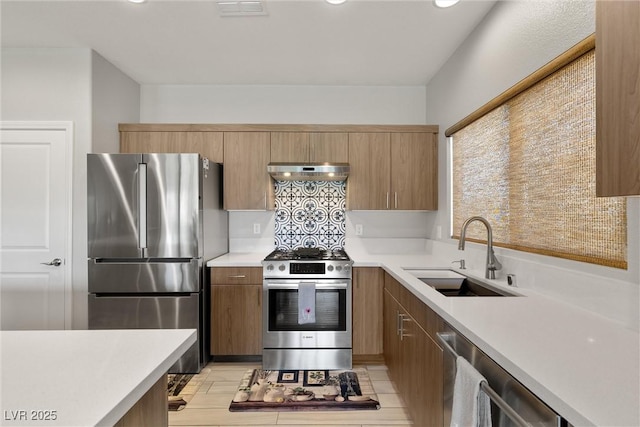 kitchen with stainless steel appliances, under cabinet range hood, light countertops, a sink, and visible vents