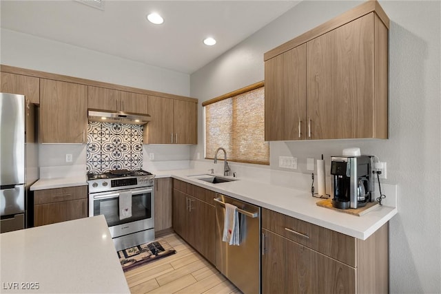 kitchen featuring a sink, under cabinet range hood, light wood-style floors, light countertops, and appliances with stainless steel finishes