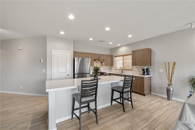 kitchen featuring a sink, a kitchen bar, light wood-type flooring, a kitchen island, and freestanding refrigerator