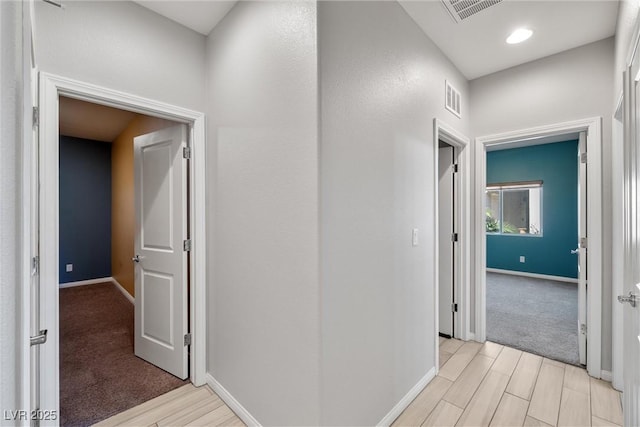 corridor with baseboards, light wood-type flooring, and visible vents