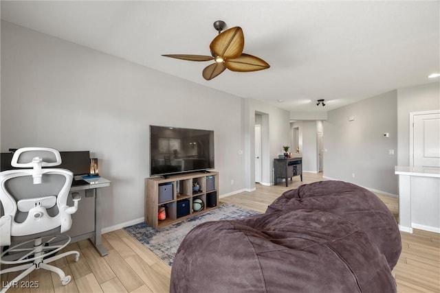 living area with baseboards, a ceiling fan, and light wood finished floors