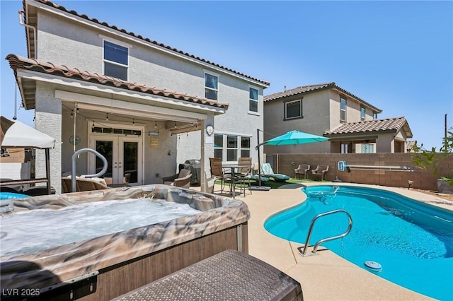 view of swimming pool with fence, a hot tub, a fenced in pool, a patio area, and french doors