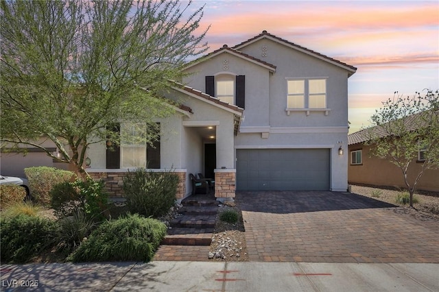 traditional-style house with a tile roof, stucco siding, stone siding, decorative driveway, and an attached garage
