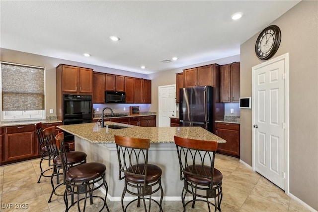 kitchen featuring a kitchen breakfast bar, a sink, black appliances, light stone countertops, and a center island with sink