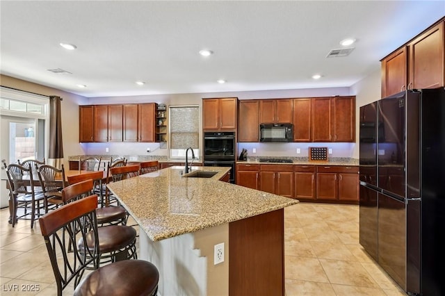 kitchen with light tile patterned floors, black appliances, a kitchen bar, and a sink
