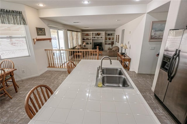 kitchen with stainless steel fridge, a fireplace, recessed lighting, tile countertops, and a sink
