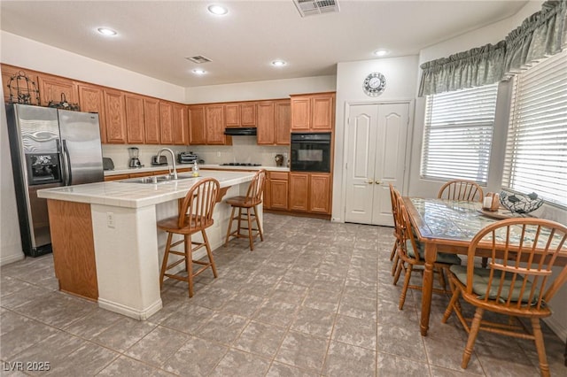 kitchen featuring oven, stainless steel fridge with ice dispenser, under cabinet range hood, a sink, and visible vents