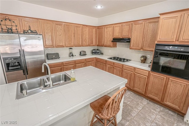 kitchen featuring a sink, gas stovetop, under cabinet range hood, stainless steel refrigerator with ice dispenser, and black oven
