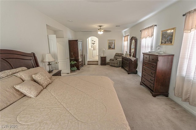 bedroom with baseboards, connected bathroom, a ceiling fan, light carpet, and arched walkways