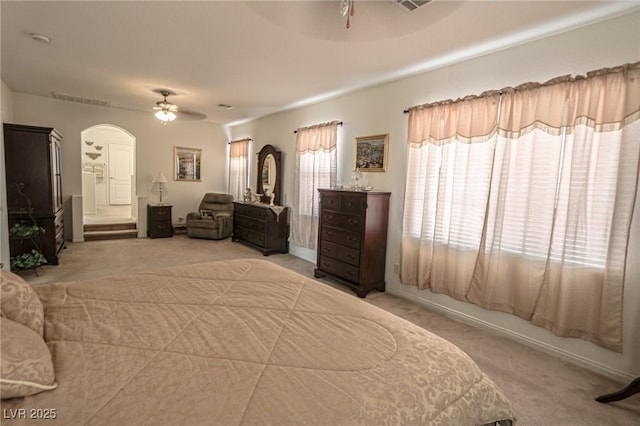 carpeted bedroom featuring arched walkways, ceiling fan, and visible vents