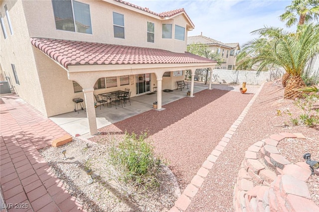 rear view of house with a tile roof, stucco siding, fence, and a patio