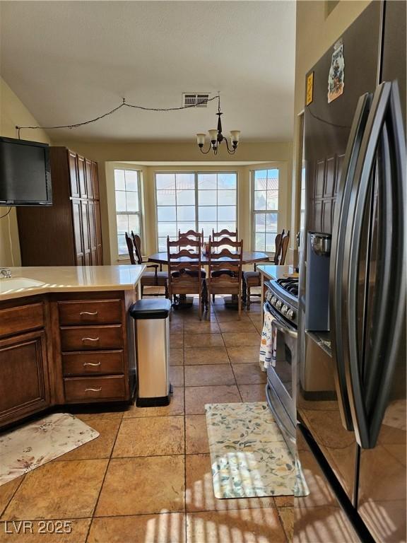 kitchen featuring light countertops, a sink, stainless steel range with gas cooktop, a notable chandelier, and black fridge