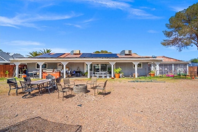 back of property with a patio, fence, a fire pit, and roof mounted solar panels