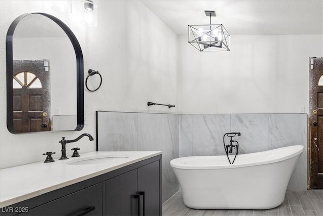 bathroom featuring a freestanding tub, tile walls, wainscoting, vanity, and a notable chandelier