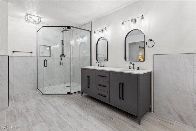 bathroom with a sink, a marble finish shower, wood tiled floor, and double vanity