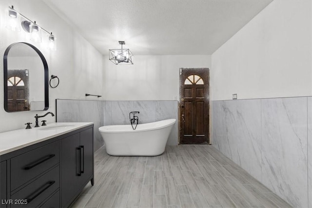 bathroom featuring vanity, wainscoting, a soaking tub, and tile walls