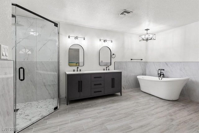 bathroom with a sink, a marble finish shower, double vanity, and a textured ceiling