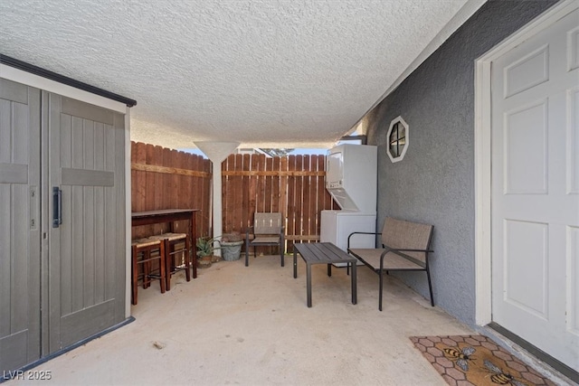 view of patio / terrace with fence and stacked washer and clothes dryer