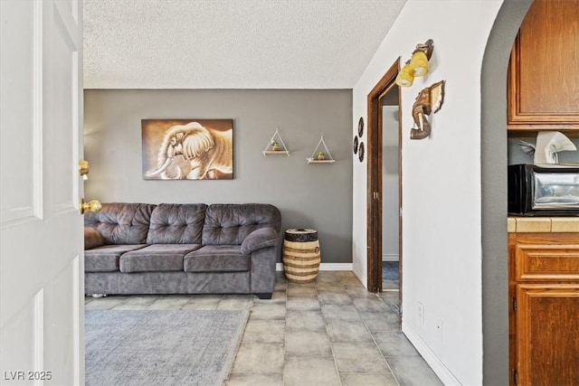 living room featuring arched walkways, a textured ceiling, baseboards, and a toaster