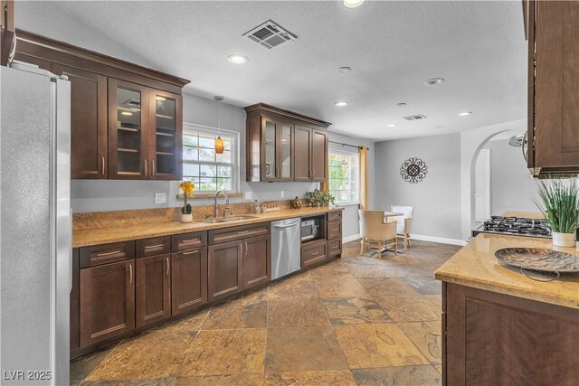 4678 Saddle Pl, Las Vegas, NV 89119 - kitchen featuring appliances with stainless steel finishes, a sink, stone tile flooring, arched walkways, and glass insert cabinets