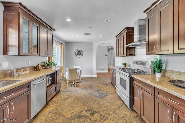 4678 Saddle Pl, Las Vegas, NV 89119 - kitchen with appliances with stainless steel finishes, arched walkways, wall chimney range hood, stone tile floors, and recessed lighting