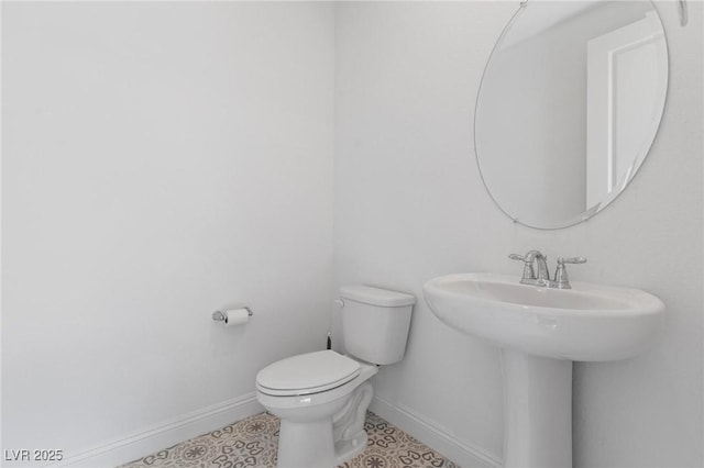 half bath featuring toilet, tile patterned floors, a sink, and baseboards