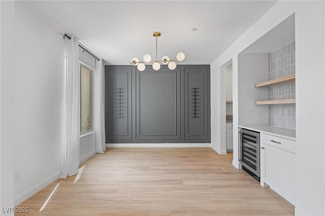 unfurnished dining area with a bar, light wood-style floors, baseboards, and wine cooler