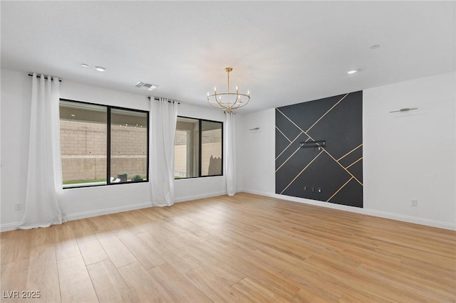 empty room with light wood finished floors, a notable chandelier, baseboards, and visible vents