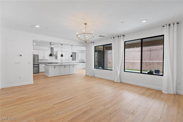 unfurnished living room with light wood-type flooring, baseboards, a chandelier, visible vents, and a sink