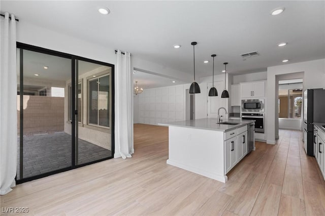 kitchen with light wood-style flooring, white cabinets, visible vents, stainless steel appliances, and a sink