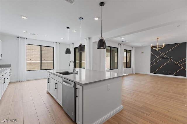 kitchen with a notable chandelier, a sink, a kitchen island with sink, light wood finished floors, and stainless steel dishwasher