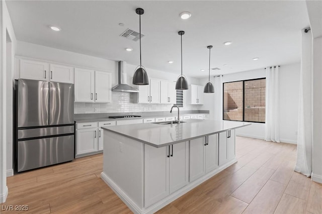 kitchen featuring freestanding refrigerator, visible vents, wall chimney exhaust hood, black cooktop, and a sink